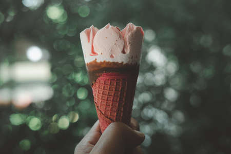 Ice cream strawberry wafer in hand against on nature blur background. Close upの写真素材