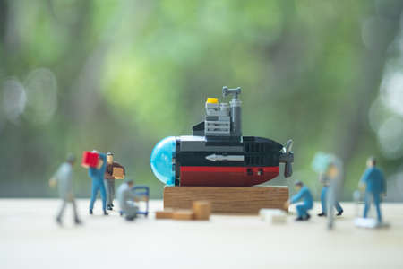 Miniature people of worker loading thing to submarine on wood table with nature background. Selective focusの写真素材