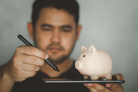 Asian man use digital pen drawing tablet with pink piggy on top. Concept of drawing the futureの写真素材