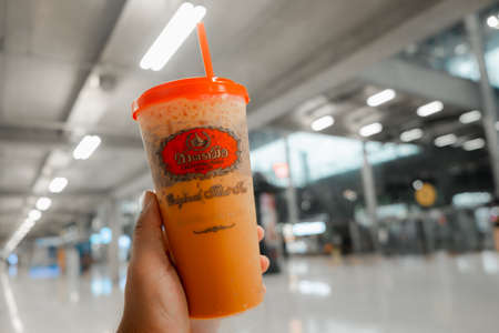 Bangkok, Thailand - September 21, 2020 : Close up hand holding a glass of iced Thai milk tea from the famous of Thai tea branding Cha Tra Mue, popular Thai tea brand and specialty tea productsのeditorial素材