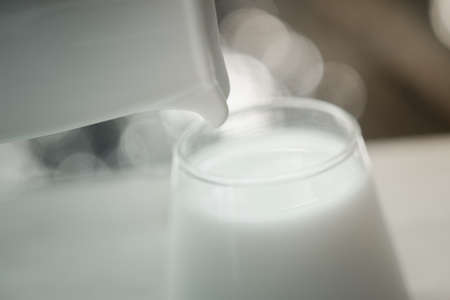 Pouring fresh milk in the glass on the wooden table with bokeh background of natureの写真素材