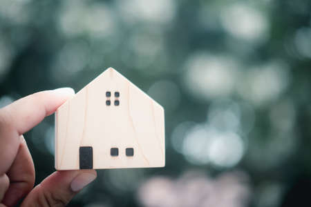 Man hand holding wooden miniature on blurred background. The concept of buying or renting real estateの写真素材