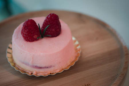 Pink mousse cake covered with pink cream rose on top with berry on a round wooden stand