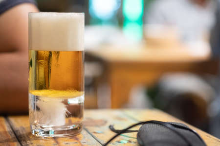 Mug of light beer pills with foam on a wooden table in a restaurant