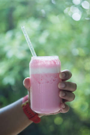 Holding a glass of pink fresh milk with blur of nature background