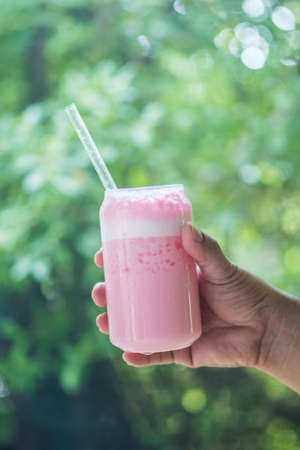 Holding a glass of pink fresh milk with blur of nature backgroundの写真素材