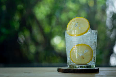 Glass of ice and slice of fresh lemon on wood table with nature background. Cold summer drinkの写真素材