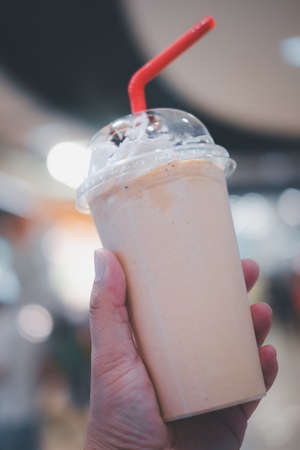 Cold cofffee blended with whipped cream on top and red tube. Close up on handの写真素材