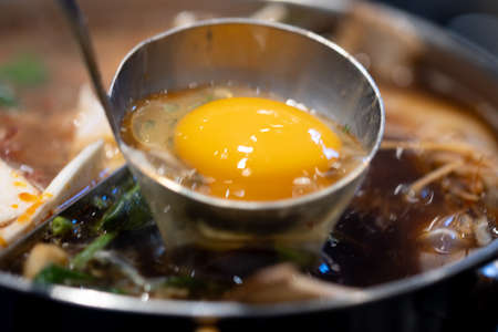 Close up of raw egg in soup ladle put into a sukiyaki pot.の写真素材