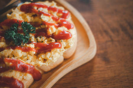 Scrambled eggs on toasted bread with ketchup on wooden trayの写真素材