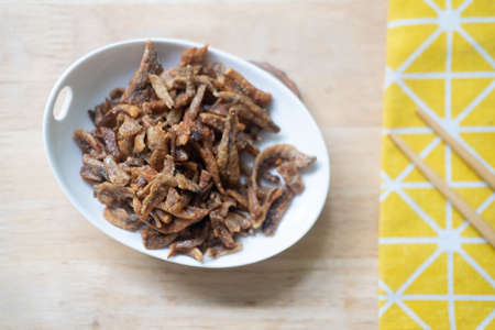 Fried crispy small fish sweet-flavored in ceramics dish with chopsticksの写真素材