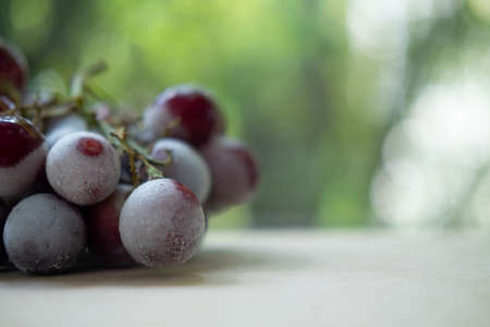 A cluster of red seedless grapes chilled on wood table. Close up with shallow depth of field and selective focus, copy spaceの写真素材