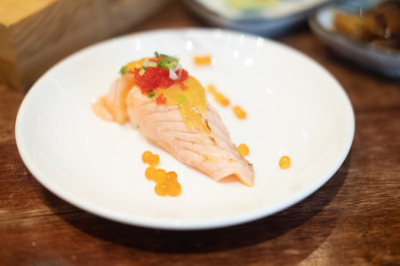 Salmon burned sushi with sauce on top with roe on white dish.の写真素材