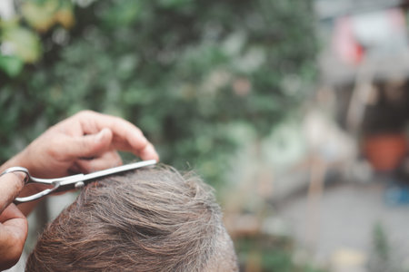 The hands of barber is cutting an Asian elderly old man with a hair cutting scissors or hair cutter comb. Healthcare and empathy concept.の写真素材