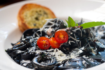 Black pasta with octopus and tomatoes on white dishの写真素材