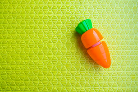 Close up of a plastic toy carrot over green background. Concept of child developmentの写真素材