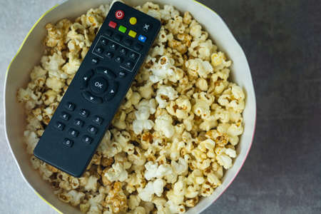 Black TV remote on popcorn in bucket. The concept of watching TV at home