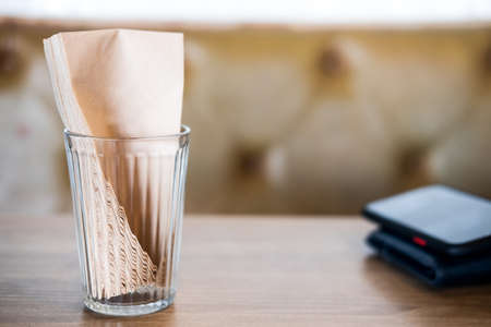 Selective focus on brown paper tissue in glass on wood table at coffee shop