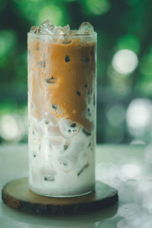 Ice coffee latte on a wooden table with coffee being poured into it showing the texture and refreshing look of the drink. Iced coffee in a tall glass.の写真素材