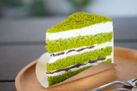 A piece triangle pandan layer cake filled with cream and red beans on wooden dish.