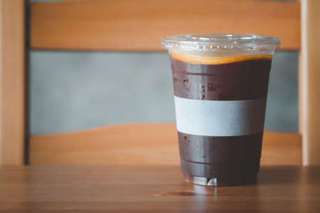 Iced black coffee topping with orange slice put on wood table.