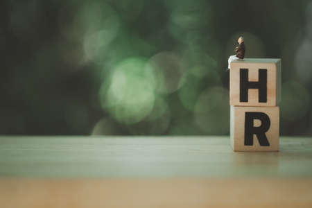 Miniature people sitting on wood blocks,with letters H and R, spelling is Human Resource against on a nature background. Concept of Human resource managementの写真素材