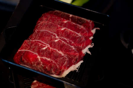 Raw freshly thin beef prepared for hot pot and Japanese sukiyaki served on black trayの写真素材