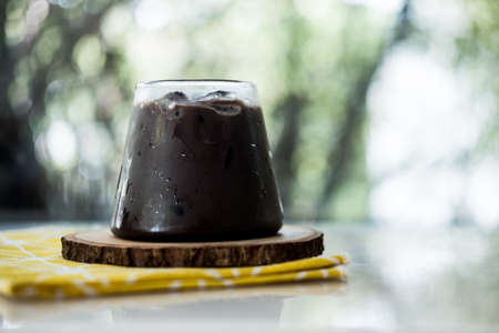 A delicious tasty dark cocoa with ice in glass on wooden saucer against nature backgroundの写真素材