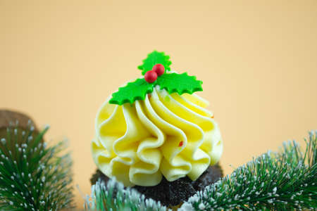 Christmas cupcakes with holly berry on a light yellow backgroundの写真素材
