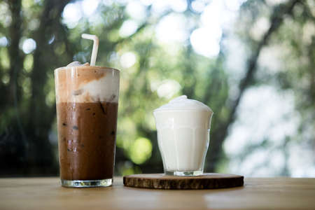 Iced Mocha coffee topping with milk foam and served with milk foam in small glass on wood tableの写真素材