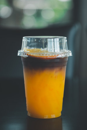A glass of coffee mixed with orange juice placed on a wooden table in cafeの写真素材