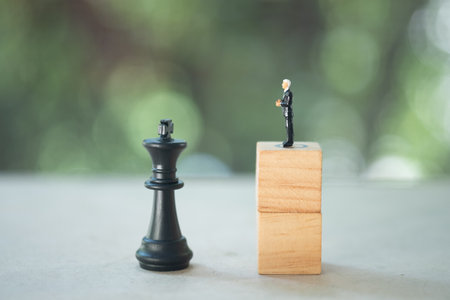 Miniature people businessman standing on wood block face to face with king chess piece. Leader concept for successの写真素材