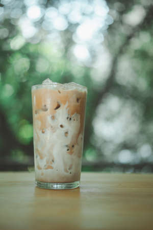 Iced coffee on a wood table with fresh milk being poured into it showing the refreshing drink with a nature backgroundの写真素材