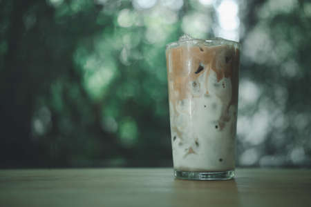 Iced coffee on a wood table with fresh milk being poured into it showing the refreshing drink with a nature backgroundの写真素材