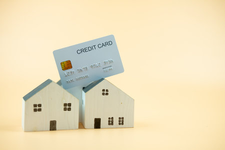 White miniature wooden house model with credit card on a yellow background. Property investment and financial conceptの写真素材