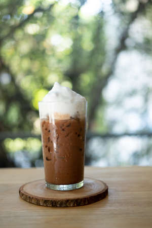 A glass of iced mocha coffee with milk foam, espresso mixed with chocolate or cocoa topped with milk foam on table at coffee cafe.の写真素材