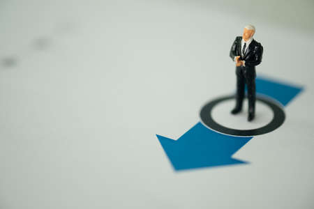 Miniature businessman standing thinking and looking on arrow pathway. Business decision concept.