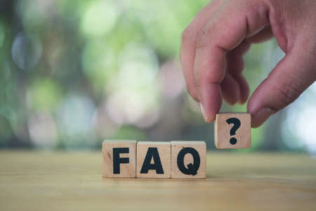 Man hand puts wooden cubes with question marks near the word FAQ. Collection of frequently asked...