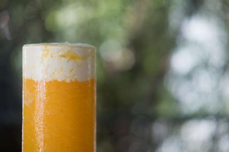 Close up of healthy smoothie orange juice in a stemless glass with milk cream on top