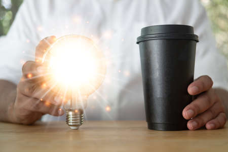 Young man holding a shining light bulb and holding a cup of hot coffee. Idea and innovation concept....