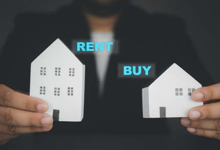 Businessman hand holding white home with text RENT and BUY for customer choice. The concept of real estate businessの写真素材