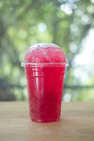 Iced red soda sweet drink in plastic glass on wood tableの写真素材