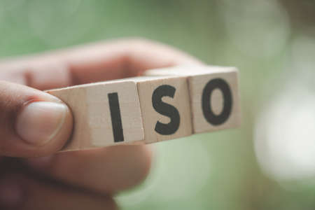 ISO acronym or International Organization for Standardization on wooden blocks in hand. Selective focusの写真素材