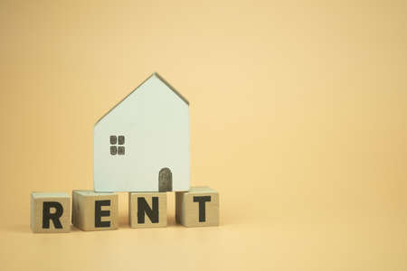 Wooden blocks with the letters RENT with wood home on top with a yellow background. Home rent conceptの写真素材