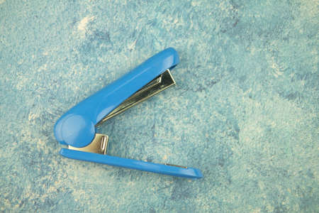 Blue office stapler on blue background. The concept of office supplies.
