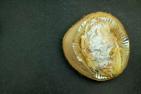 Almond croissant with almond flakes and powdered sugar in foil cup on a wooden chopping board