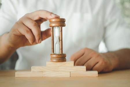 Businessman in white shirt holds an hourglass on wooden block. Concept of time and Business time...