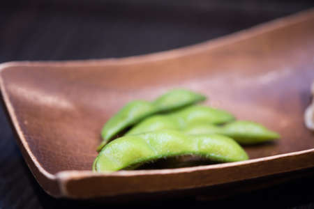 Edamame or green soybeans blanched in wood bowl on wooden table at japanese restaurant.