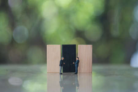 Miniature businessman shaking hands with wooden domino against nature backgroundの写真素材