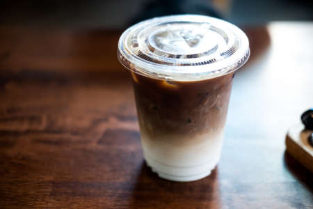 Iced latte coffee with fresh milk layer in takeaway glass on wood table
